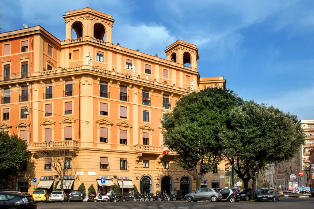 Nell'immagine, l'esterno dell'Hotel Astrid: si vede il palazzo da lontano e la strada con delle macchine.